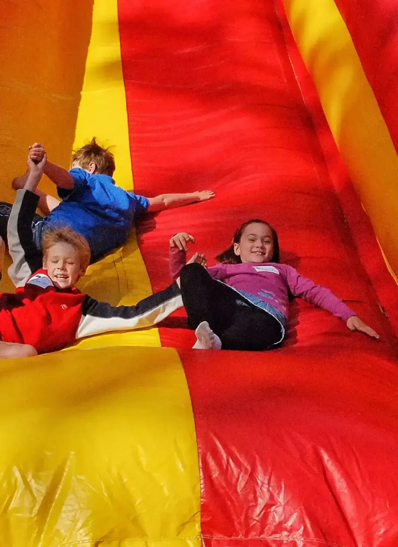 happy-kids-2023 Three children sliding in an inflatable bouncing slide.