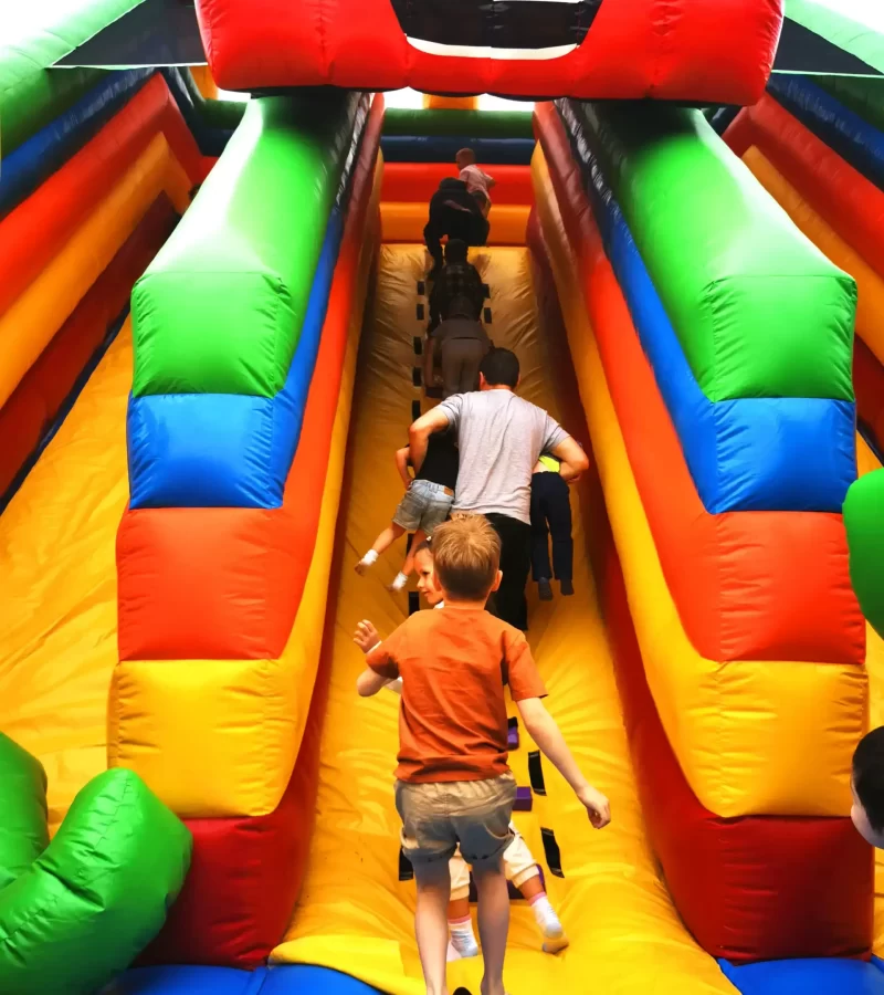 rear-view-many-children-climb-the-slide-on-a-color A rear view of children and a dad carrying his kids climbing back to the bouncing slide.